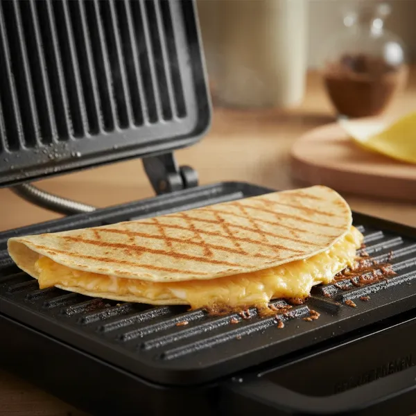 Golden-brown quesadilla with melted cheese being grilled on a George Foreman grill, showing grill marks.